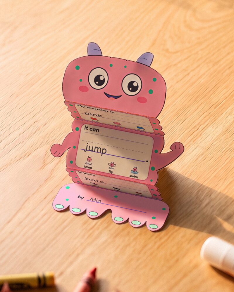 My Monster Grows writing craft standing on a table: a pink spotted monster folded like a fan, with pink, jump and bats written in its sentence frames and by Mia on its feet